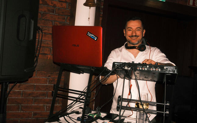 DJ mit Laptop und Mixer auf kleiner Bühne, Industrial-Location.