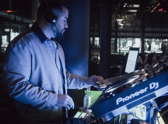 DJ im blauen Licht mischt live am Controller, Seitenansicht.